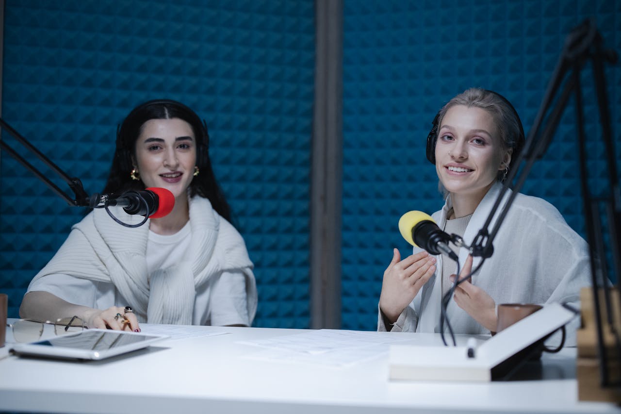 Two women podcasters engaging in discussion inside a modern recording studio with microphones.